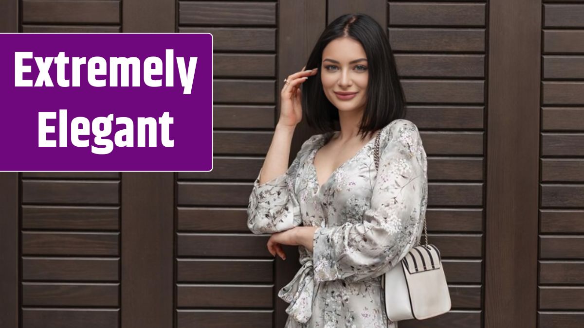 Happy beautiful fashionable young elegant woman with a smile in a fashion summer dress with a floral pattern with a stylish white handbag stands near a wooden door on the street.